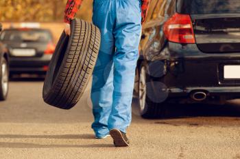 Male worker in uniform holds tyre, tire service. Vehicle repair service or business, man repairing broken wheel