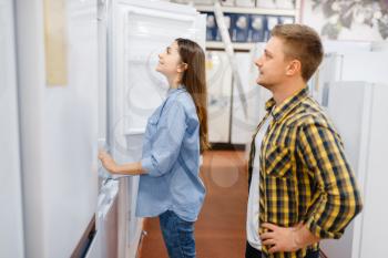 Family couple choosing refrigerator in electronics store. Man and woman buying home electrical appliances in market