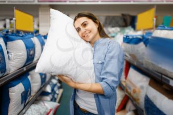 Young woman with pillows in bed linen store. Female person buying home goods in market, lady in bedding shop