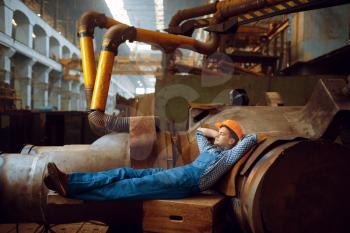 Male worker in uniform and helmet resting at lunchtime on factory. Metalworking industry, industrial manufacturing of steel products