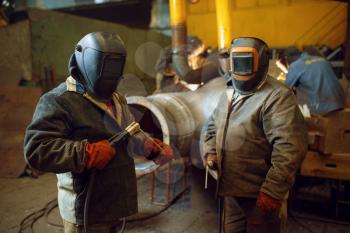 Two welder in masks prepares to work with metal construction on factory, welding skill. Metalworking industry, industrial manufacturing of steel products
