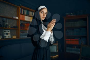 Young nun in a cassock with a cross around her neck holds a book. The sister is preparing for prayer in the monastery