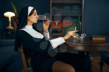 Sexy nun in a cassock sitting in a depraved pose with cigarette and glass of wine, vicious desires. Corrupt sister in the monastery, religion and faith, sinful religious people, attractive sinner