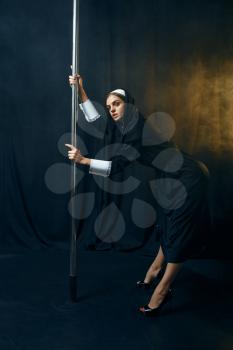 Sexy nun in a cassock dances on a pole like a stripper, vicious desires. Corrupt sister in the monastery, sinful religious people, attractive sinner