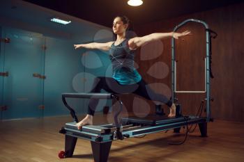 Slim girl in sportswear keeps the balance, pilates training on exercise machine in gym. Fitness workuot in sport club. Athletic female person, aerobics indoor, body stretching