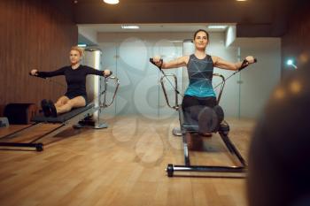 Two women in sportswear, pilates training on exercise machine in gym. Fitness workuot in sport club. Athletic female person, aerobics indoor, body stretching