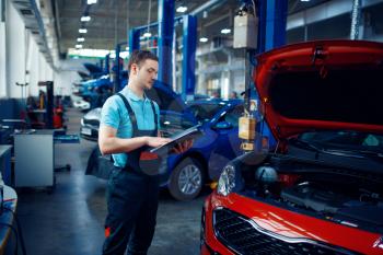 Worker with a checklist stands at vehicle with opened hood, car service station. Automobile checking and inspection, professional diagnostics and repair