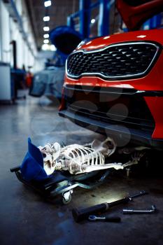 Human skeleton lying under the vehicle, car service station, problematic vehicle concept. Automobile checking and inspection, professional diagnostics and repair