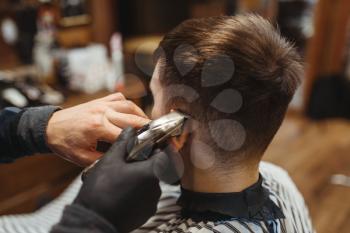 Barber holds comb and cuts the client 's hair. Professional barbershop is a trendy occupation. Male hairdresser and customer in retro style salon
