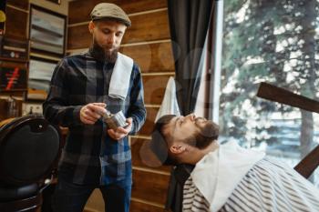 Barber with brush and bearded customer, beard cutting. Professional barbershop is a trendy occupation. Male hairdresser and client in hair salon