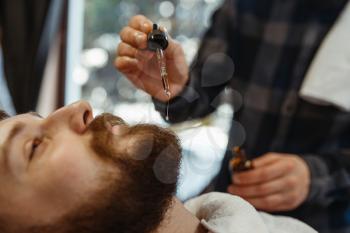 Barber and customer, beard cutting closeup. Professional barbershop is a trendy occupation. Male hairdresser and client in hair salon