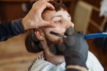 Barber with razor, old school beard cutting. Professional barbershop is a trendy occupation. Male hairdresser and client in hair salon