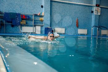 Female swimmer in swimsuit, cap and glasses swims butterfly in pool. The woman in the water, sport swimming training, motion view