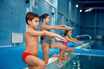 Children swimming group, workout at the poolside. Kids learns to swim in the water, sport training, fitness exercise in the pool