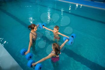 Children swimming group, workout with dumbbells in the pool. Kids learns to swim in the water, sport training, fitness exercise