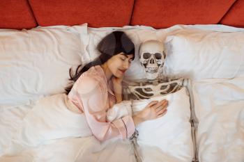 Woman and human skeleton sleeping in the bed, bad relationship. Couple having a problems, family quarrel or conflict