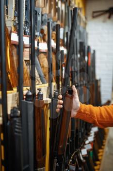Man choosing rifle at showcase in gun shop. Euqipment for hunters on stand in weapon store, hunting and sport shooting hobby