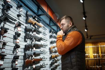 Man looking on handguns on showcase in gun shop. Euqipment for hunters on stand in weapon store, hunting and sport shooting hobby