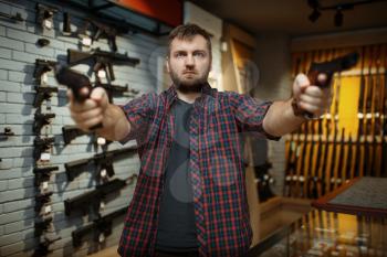 Man aims with two handguns in gun shop. Male person buying pistol for security in weapon store, selfdefence and sport shooting hobby