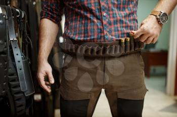 Man choosing ammo belt and uniform for hunting in gun shop. Euqipment for hunters on stand in weapon store, sport shooting hobby