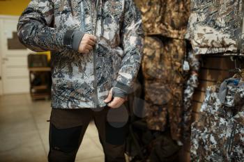 Man trying on uniform at showcase in gun shop. Euqipment and rifles for hunters on stand in weapon store, hunting and sport shooting hobby