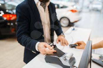 Man pays for the purchase of a new auto in car dealership. Customer and saleswoman in vehicle showroom, male person buying transport, automobile dealer business