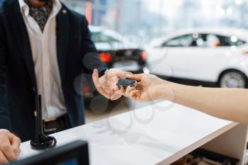 Man takes the key from new auto in car dealership. Customer and saleswoman in vehicle showroom, male person buying transport, automobile dealer business