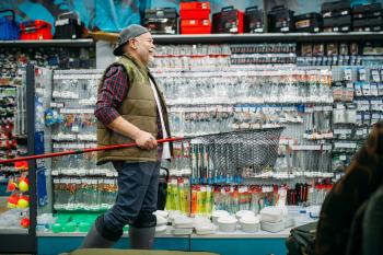 Fisherman with net and toolbox in fishing shop, hooks and baubles on background. Equipment and tools for fish catching and hunting, accessory choice on showcase in store, bait assortment