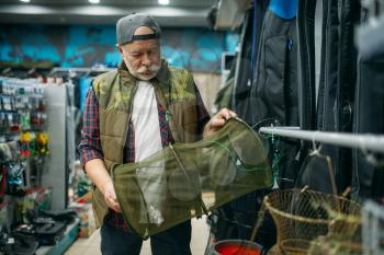 Male angler choosing net in fishing shop, hooks and baubles on background. Equipment and tools for fish catching and hunting, accessory choice on showcase in store, bait assortment