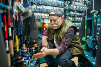 Fisherman choosing reel in fishing shop. Male angler buying equipment and tools for fish catching and hunting, accessory choice on showcase in store