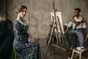 Portrait painter with palette and brush draws female model. Man sitting at the easel, art studio interior on background