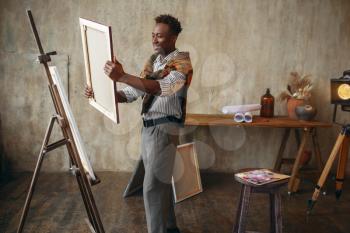 Smiling painter with canvas standing near the easel. Male artist draws at his workplace, creative master works in workshop
