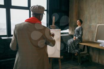 Portrait painter with brush draws female model. Male artist standing at his workplace, creative master at the easel in workshop