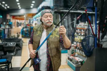 Male angler puts the line in the eye of the rod in fishing shop. Equipment and tools for fish catching and hunting, accessory choice on showcase in store