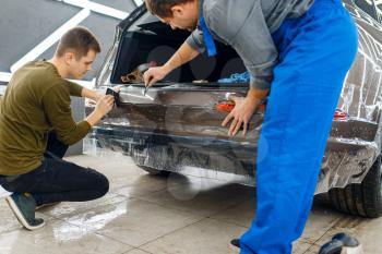 Specialists applies car protection film on rear bumper. Installation of coating that protects the paint of automobile from scratches. New vehicle in garage, tuning procedure