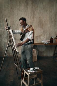 Happy painter prepares easel with canvas in art studio. Male artist draws at his workplace, creative master works in workshop