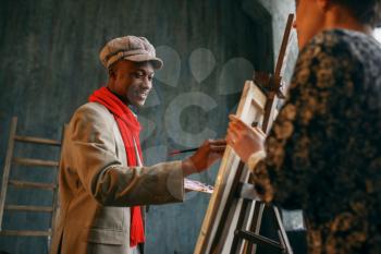 Portrait painter at the easel draws female model. Male artist standing at his workplace, creative master works in workshop