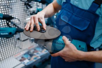Male worker in uniform choosing edged disc for angle grinder in tool store. Choice of professional equipment in hardware shop, instrument supermarket