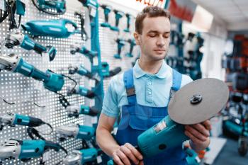 Male worker in uniform holds angle grinder in tool store. Choice of professional equipment in hardware shop, instrument supermarket