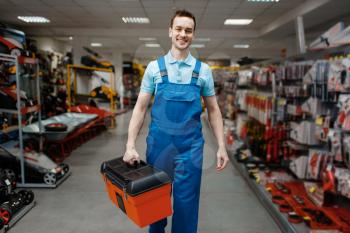 Smiling male worker in uniform buying toolbox in tool store. Choice of professional equipment in hardware shop, instrument supermarket