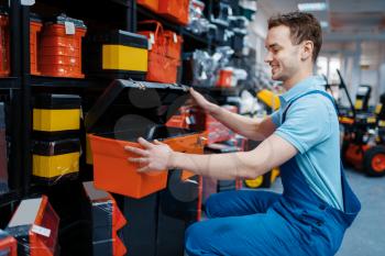 Male employee in uniform choosing toolbox in tool store. Choice of professional equipment in hardware shop, instrument supermarket