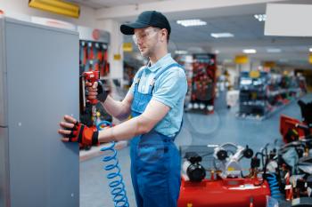 Male worker in uniform testing pneumatic nailer in tool store. Choice of professional equipment in hardware shop, instrument supermarket