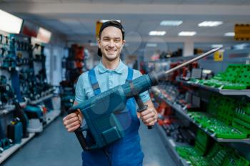 Male worker holds big electric perforator in tool store. Choice of professional equipment in hardware shop, electrical instrument supermarket