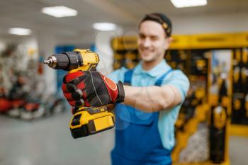 Male worker holds battery powered screwdriver in tool store. Choice of professional equipment in hardware shop, electrical instrument supermarket