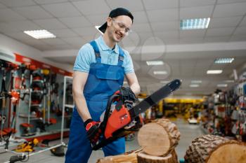 Male worker in uniform testing chainsaw in tool store. Choice of professional equipment in hardware shop, electrical instrument supermarket