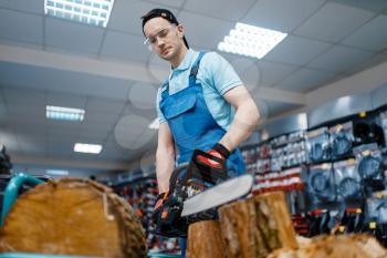 Male worker in uniform testing chainsaw in tool store. Choice of professional equipment in hardware shop, electrical instrument