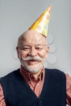 Portrait of smiling elderly man in party cap isolated on grey background. Cheerful mature senior looking at camera in studio