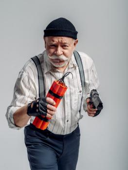 Elderly robber poses with dynamite and gun on grey background, gangster. Mature senior in studio, man in old age