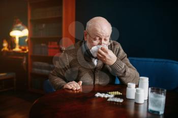 Sick elderly man blows his nose in a handkerchief in home office, age-related diseases. Mature senior is ill and being treated in his house