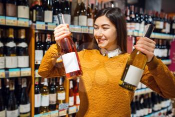 Woman with two bottles of alcohol in grocery store. Male person buying beverages in market, customer shopping food and drinks